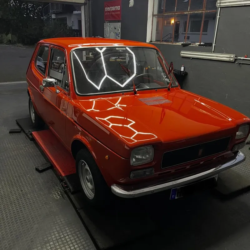 Oranger Fiat 127 auf der Hebebühne unter dem Wabenlicht
