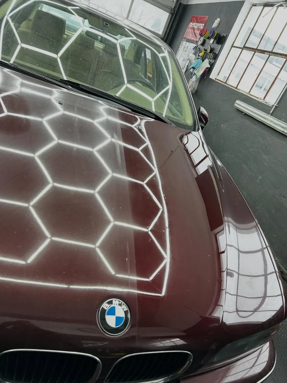 Wabenlicht der Werkstatt spiegelt sich in der frisch polierten weinroten Motorhaube